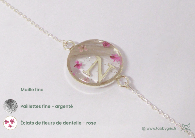 Bijou en crins de cheval avec une initiale P au milieu, deux mèches de crins de chaque côté et des éclats de fleurs de dentelle rose.